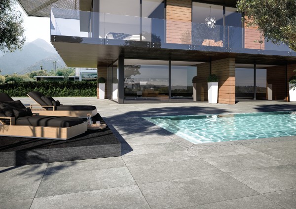 Contemporary backyard with a pool surrounded by large gray porcelain pavers, modern lounge chairs, and a sleek home with glass balcony, creating a clean and stylish outdoor living area.