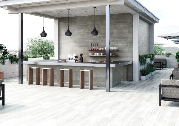Outdoor bar and seating area with wood-look exterior tile flooring, modern pendant lights, and sleek bar stools under a covered patio.