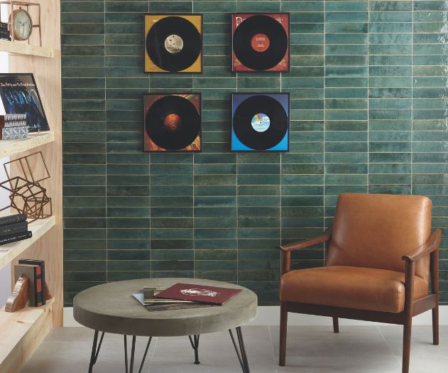 A contemporary living room featuring a green tiled wall with mounted vinyl records, a brown leather chair, and a minimalist round coffee table with books.