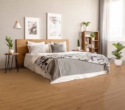 A stylish bedroom featuring a wooden headboard and flooring, with plants and framed art as decorations.