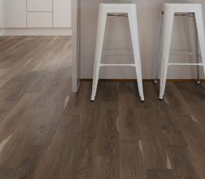 A modern kitchen with white stools and wooden flooring.