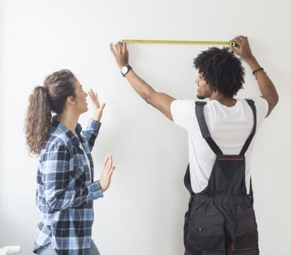 A man and a woman begin measuring their room prior to a home remodel