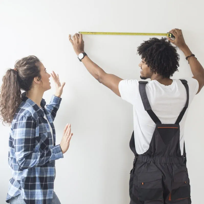 A man and a woman begin measuring their room prior to a home remodel