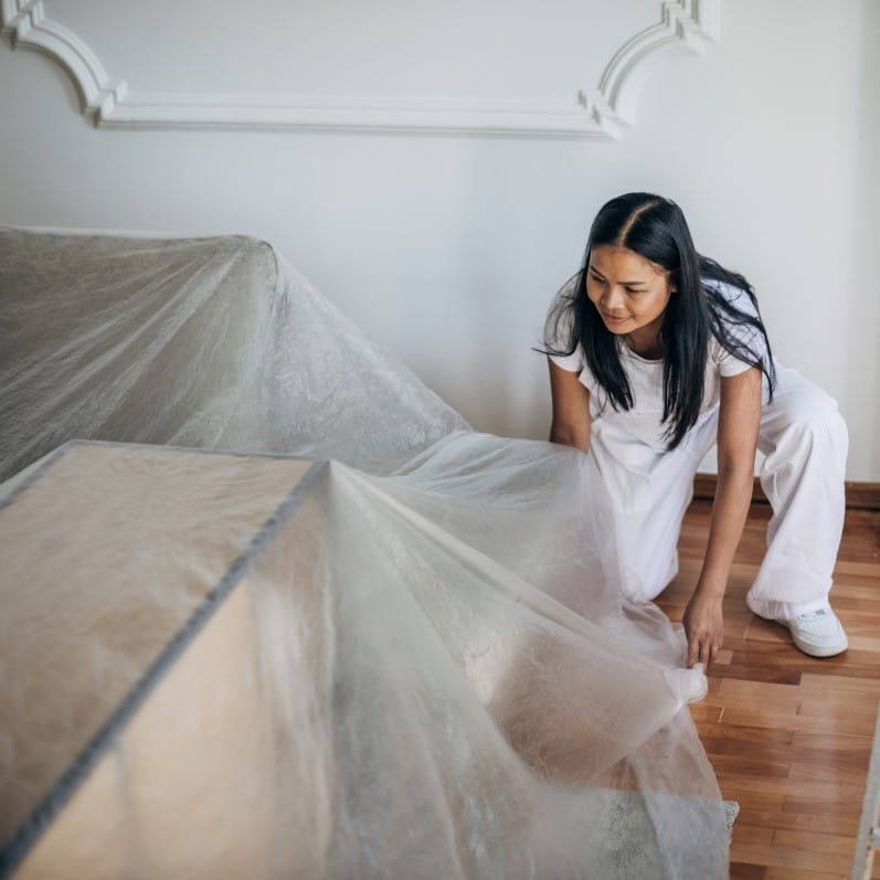 A woman places drop cloth over her furniture prior to a home remodel
