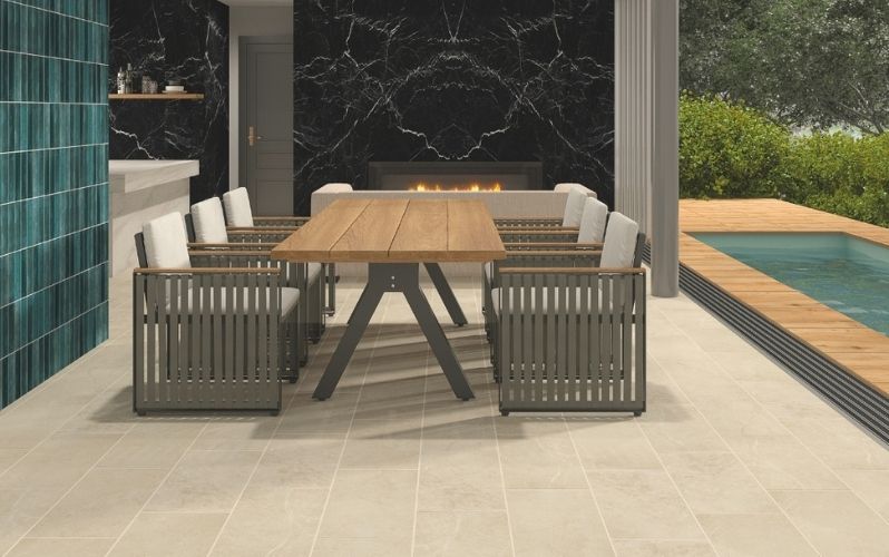 Outdoor dining area with a wooden table, chairs, a black marble fireplace, and a pool nearby.