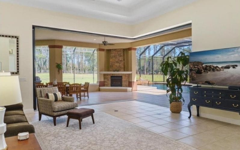 An outdoor living space showcasing a fireplace, comfortable seating, and a view of a screened enclosure and greenery.