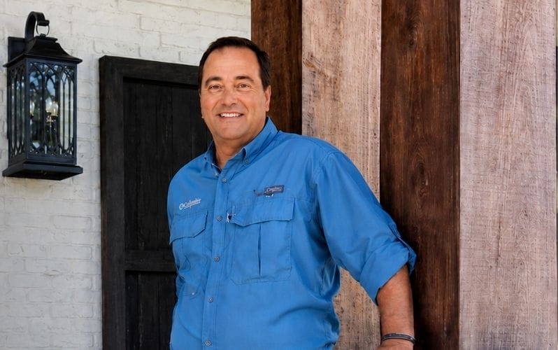 Rick Rojas in a blue short leaning on a support beam on a home he constructed