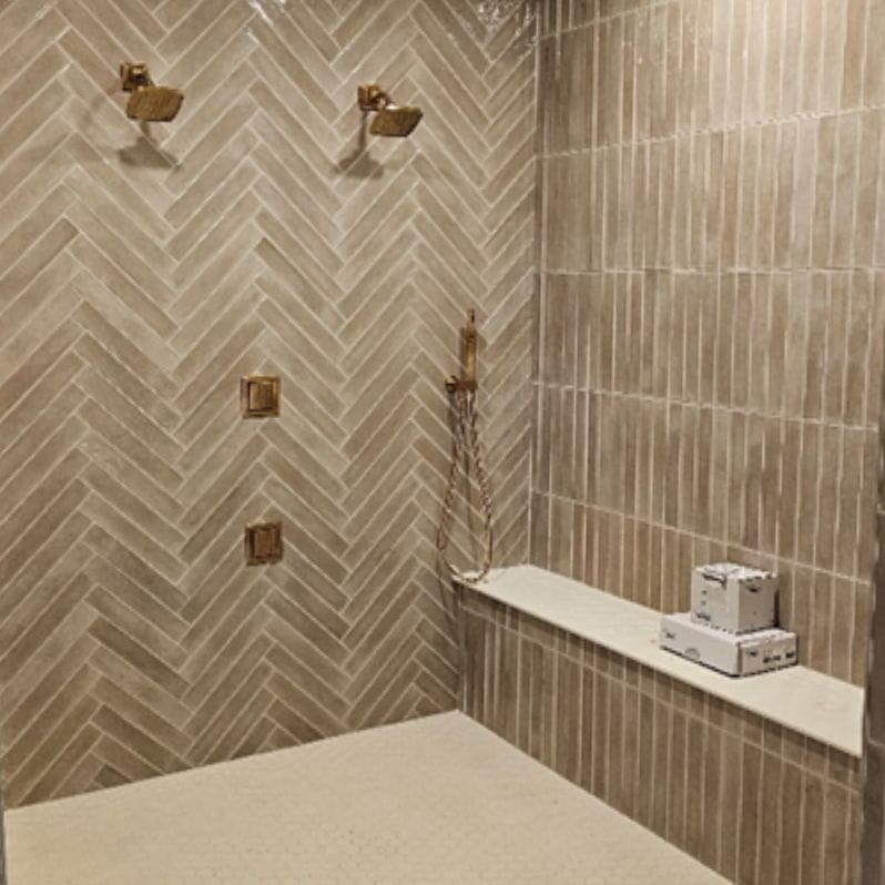 A spa-inspired walk-in shower with brass hardware and stunning neutral tone high gloss tiled walls in both a herringbone and vertical pattern.