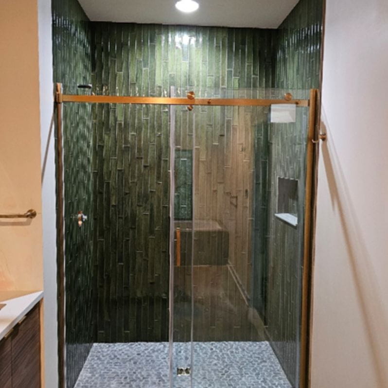A modern walk-in shower with vivid emerald vertical tiles and copper hardware.