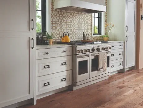 Stylish kitchen with white shaker cabinets, geometric backsplash, stainless steel range, and Atlas Homewares black rectangular pulls