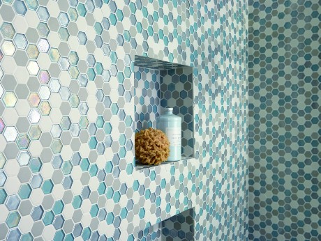 Shower wall with glossy blue, aqua, and white hexagon mosaic tiles, featuring built-in recessed shelves holding a sponge and bath product for a functional and stylish accent.