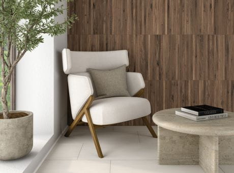 A modern living area with a white armchair, wooden wall paneling, a concrete table, and a potted plant by the window.