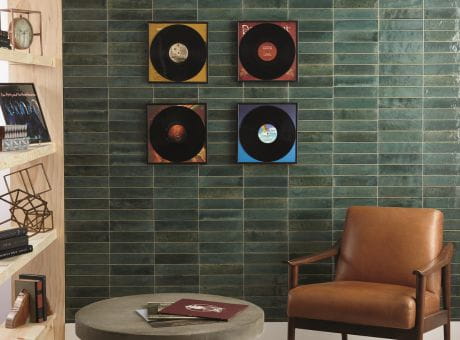 Living room area with green tiled wall, vinyl record decor, leather chair, circular ottoman, and wooden shelves.