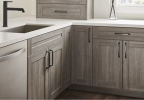 Modern gray-toned kitchen cabinets with black hardware, white countertop, and stainless steel appliances.