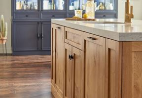 Modern kitchen interior with wooden island, light countertop, and dark blue cabinet in the background.