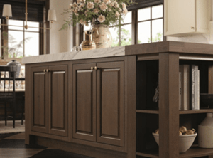Wooden kitchen island with marble top, brass handles, and decorative vase with flowers.