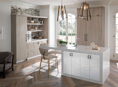 A modern kitchen with a central island, wooden cabinetry, pendant lights, and herringbone flooring.