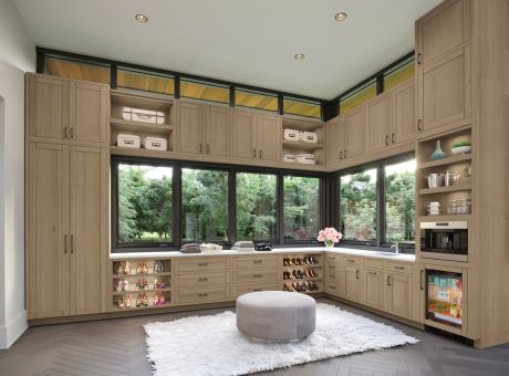 Interior view of a modern walk-in closet with wooden cabinetry, large windows, and a central ottoman.