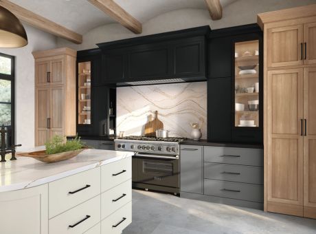 A modern kitchen featuring black and light wood cabinetry, a stove with a hood, and a marble backsplash under a high ceiling with exposed beams.