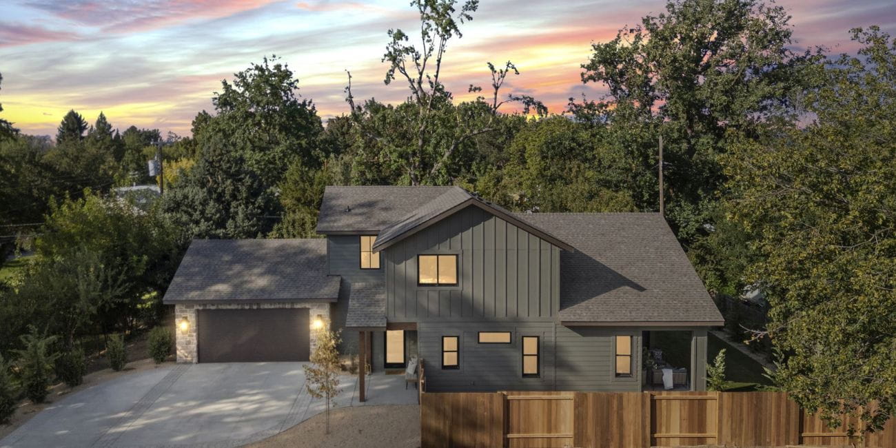 Exterior of The Audrey a custom home built by MVMNT Homes. A modern farmhouse with darker paneling and a multi car garage nestled in a wooded area.