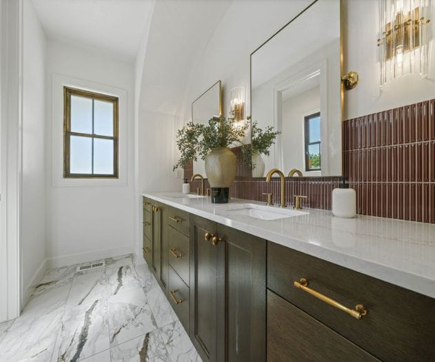 A beautiful rust color tile backsplash with white marble floors against a deep wood bathroom cabinets
