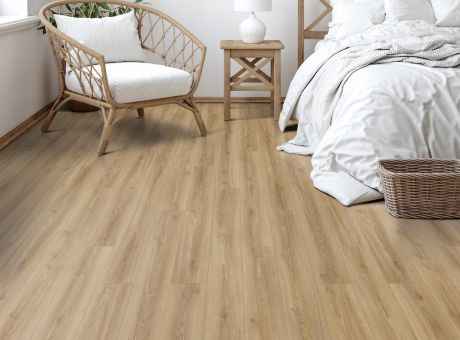 Bedroom with light wood laminate flooring, rattan chair, and white linens.