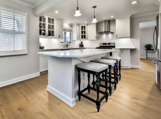 Kitchen interior with RevWood Castlebriar flooring, white cabinets, island with stools, and stainless steel appliances.