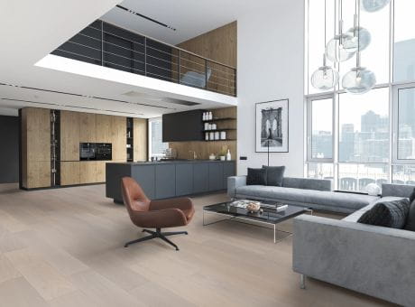 A modern loft apartment with an open-concept kitchen and living area, furnished with a brown leather chair, grey sofa, and minimalist decor.