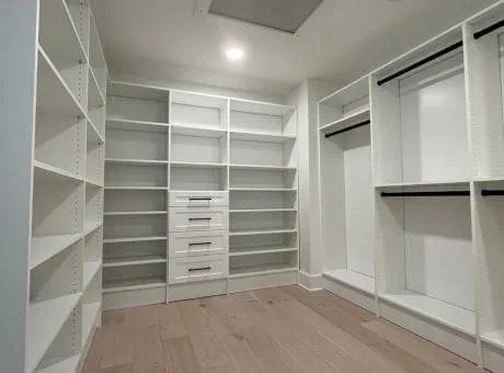 Walk-in closet featuring white shelves, hanging spaces, and drawers, with wooden flooring.