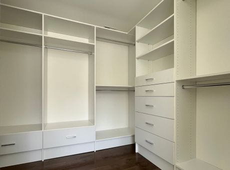 A white closet interior with shelves, drawers, and rods for clothing organization.