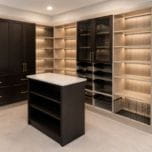 Well-designed walk-in closet featuring illuminated shelving, dark wooden cabinetry, and a central island with a white countertop.