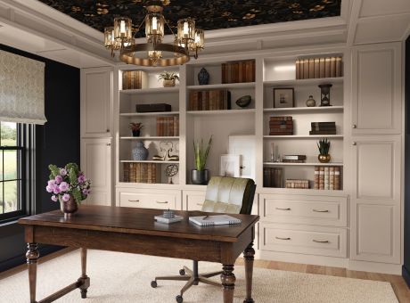 Traditional home office with white built-in bookshelves, a dark wood desk, rolling chair, window, and chandelier-style ceiling light.