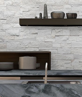 Modern kitchen with a gray marble countertop and stainless steel sink, featuring a white stacked stone backsplash and a floating shelf with minimalist decor.