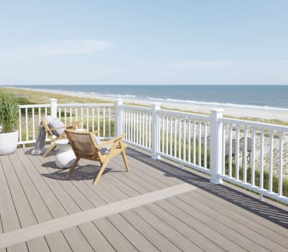 Beachfront deck with light wood composite decking, white TimberTech railing, two wooden chairs facing the ocean, and a clear blue sky.
