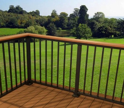 Corner view of a deck with brown composite decking and black Westbury aluminum railing, overlooking a large green lawn and trees.