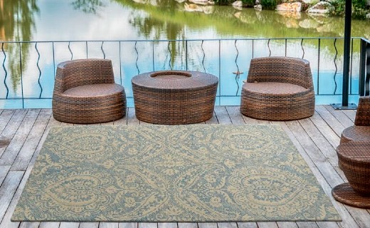 Outdoor deck overlooking a pond with three woven rattan chairs and a matching round table centered on a blue and beige paisley-patterned area rug.