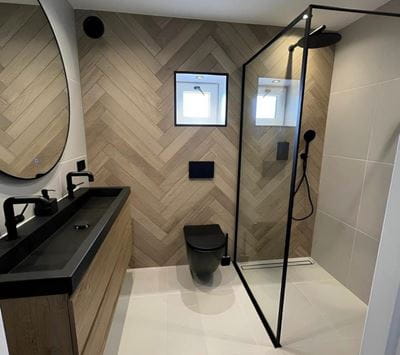 Herringbone tile walls with a bathroom vanity, shower, and lighted mirror