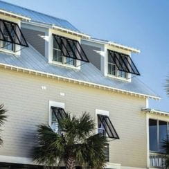 Exterior of a light-colored building with black awning shutters on multiple windows and palm trees nearby.