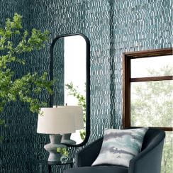 Textured blue wallpaper in a living room with an arched mirror, lamp, chair, and window.