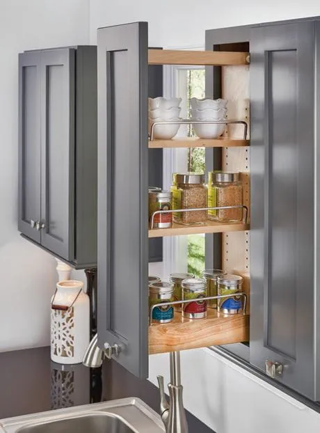 Kitchen wall pull-out organizer holding spices and dishes within a grey cabinet.