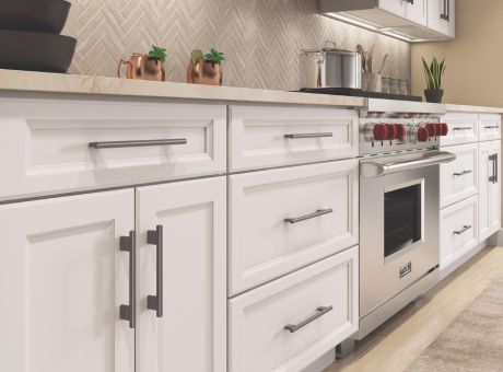 A modern kitchen with white cabinets, a stainless steel oven with red knobs, and decor items like plants and mugs.