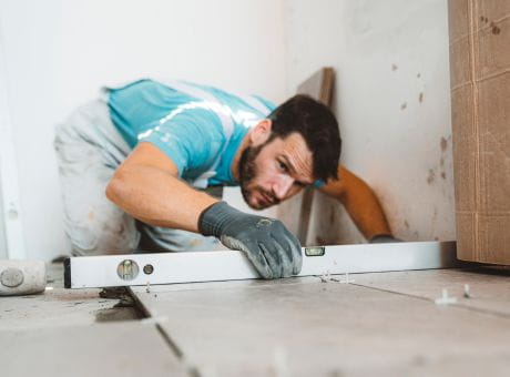 A worker installing tiles on the floor and accurately aligning them with a spirit level.