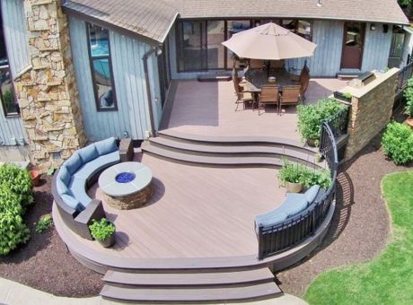 A wooden deck with curved steps, a circular seating area with a fire pit, and an outdoor dining table under an umbrella.
