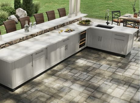 Outdoor kitchen with white cabinets, a sink, and a seating area overlooking a grass field.