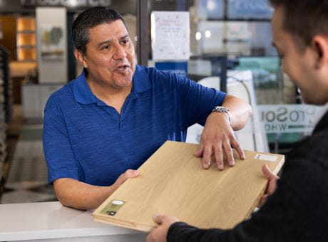 Two individuals interacting across a store counter, exchanging a wooden sample board.