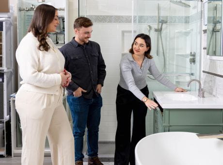 Two women and a man in a bathroom showroom examining furniture and discussing details.