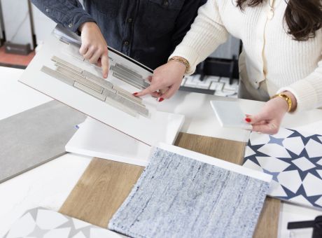Two individuals reviewing material swatches and patterns for an interior project, focusing on tiles and textures.