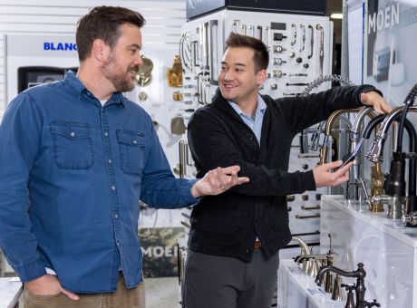 Two people discussing faucets in a kitchen hardware store, surrounded by various hardware displays.