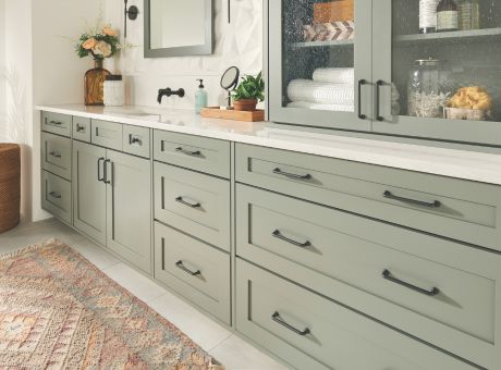 Modern kitchen featuring sage green cabinets with black handles, countertop with decorative items, and a textured rug.