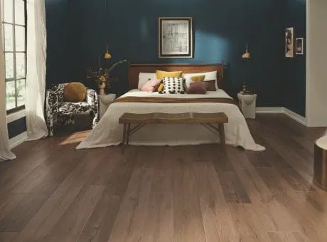 Bedroom with hardwood flooring and modern decor, including a wooden bed, colorful pillows, and a decorative chair.